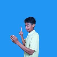 excited asian man wearing yellow t-shirt pointing to the copy space on the side blue background. photo