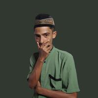 Asian man wearing green muslim shirt on green background, asking for silence with finger on lips. suitable for the Ramadan theme. photo