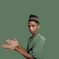 excited asian man wearing ramadan muslim clothes. pointing to copy space with side blue background. photo