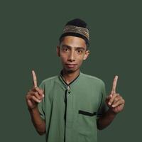 excited asian man wearing ramadan muslim clothes. pointing to copy space with side blue background. photo