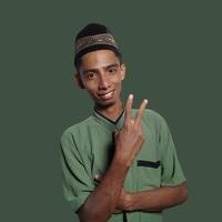 Excited Asian Muslim man wearing Muslim clothes pointing at copy space on green background. photo