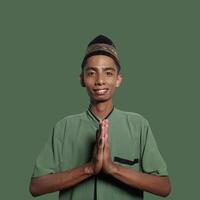 young asian man smiling during ramadan. gesturing the traditional gesture of wearing Muslim clothes. photo