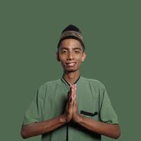 joven asiático hombre sonriente durante Ramadán. gesticulando el tradicional gesto de vistiendo musulmán ropa. foto