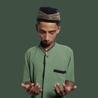 Young Asian man praying wearing green muslim clothes during ramadan green background photo