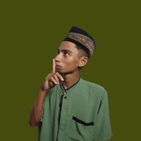 Asian man wearing green muslim shirt on green background, asking for silence with finger on lips. suitable for the Ramadan theme photo