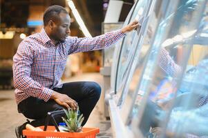 Portrait of smiling man at supermarket. Young african man with shopping basket in grocery store photo