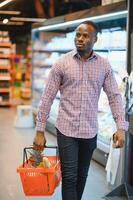 Portrait of smiling man at supermarket. Young african man with shopping basket in grocery store photo