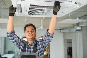 Concentrated young Indian engineer setting up air conditioner. photo