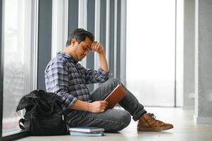 Full length of depressed boy sitting with backpack in school corridor photo