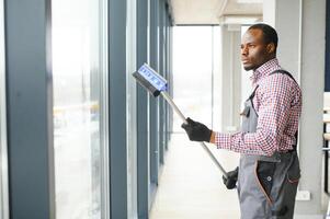 africano masculino profesional limpieza Servicio trabajador en mono limpia el ventanas y tienda ventanas de un Tienda con especial equipo foto