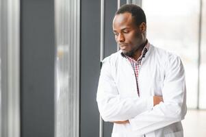 Portrait of young male doctor, standing against window at hospital corridor photo