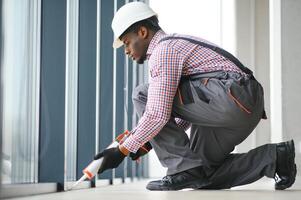 Construction african worker repairing plastic window with screwdriver indoors, space for text. Banner design photo