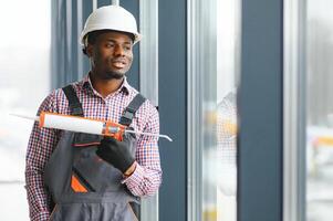 Low Angle View Of A Young African Repairman In Overalls Installing Window photo