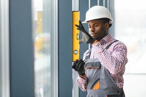 Low Angle View Of A Young African Repairman In Overalls Installing Window photo