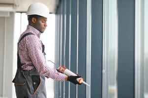Low Angle View Of A Young African Repairman In Overalls Installing Window photo
