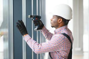 Low Angle View Of A Young African Repairman In Overalls Installing Window photo