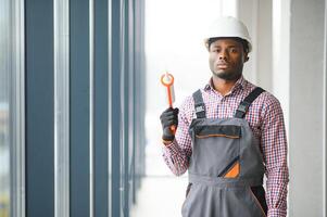 Low Angle View Of A Young African Repairman In Overalls Installing Window photo