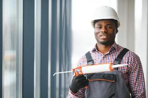 Low Angle View Of A Young African Repairman In Overalls Installing Window photo