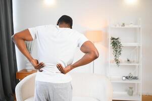 African American guy suffering from back pain, leaning on sofa, cannot walk at home photo