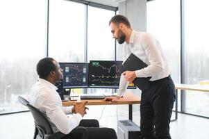 Two successful trader sitting in office, checking cryptocurrency information data on finance market graph, pointing on monitor photo