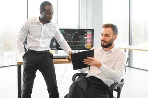 Two confident businessmen, financial analysts or investment advisers sitting at office desk photo