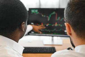 Two successful trader sitting in office, checking cryptocurrency information data on finance market graph, pointing on monitor photo