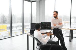 Two successful trader sitting in office, checking cryptocurrency information data on finance market graph, pointing on monitor photo