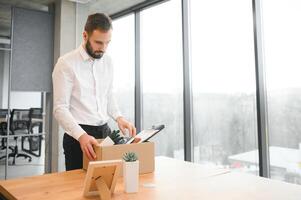 Sad Fired. Let Go Office Worker Packs His Belongings into Cardboard Box and Leaves Office. Workforce Reduction, Downsizing, Reorganization, Restructuring, Outsourcing. Mass Unemployment Market Crisis photo