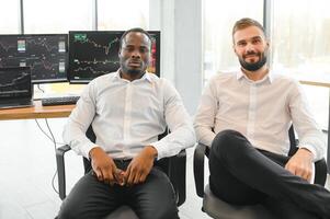 Two successful trader sitting in office, checking cryptocurrency information data on finance market graph, pointing on monitor photo