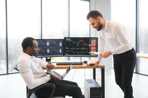 Two successful trader sitting in office, checking cryptocurrency information data on finance market graph, pointing on monitor photo