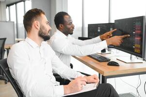 Two successful trader sitting in office, checking cryptocurrency information data on finance market graph, pointing on monitor photo