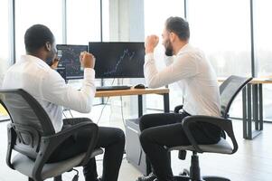 Two successful trader sitting in office, checking cryptocurrency information data on finance market graph, pointing on monitor photo