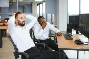 Two diverse colleagues traders talking to each other, sitting in the office in front of multiple computer screens. Stock trading, people, business concept photo