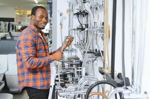 A large selection of water faucets. African american Man chooses a products in a sanitary ware store photo