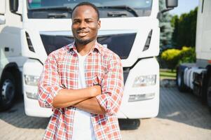 Front view. Young african truck driver is with his vehicle at daytime. photo