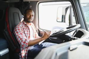 Professional african american truck driver in casual clothes driving truck vehicle going for a long transportation route. photo