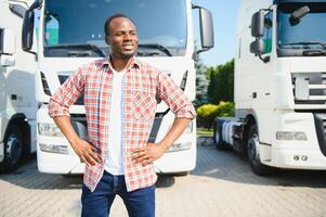 Front view. Young african truck driver is with his vehicle at daytime. photo