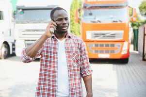 Black man truck driver near his truck parked in a parking lot at a truck stop. photo