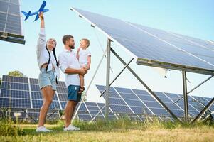 A wide shot of a happy family standing together and smiling at camera with a large solar panel in background photo