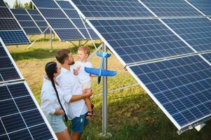 Young family with a small child in her arms on a background of solar panels. A man and a woman look at each other with love. Solar energy concept. photo