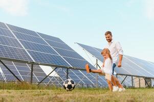 padre y hijo tener divertido jugando fútbol americano cerca el solar paneles el concepto de verde energía foto