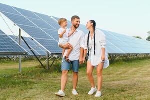 un amplio Disparo de un contento familia en pie juntos y sonriente a cámara con un grande solar panel en antecedentes foto