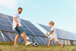 Father and son playing football in garden of solar paneled photo