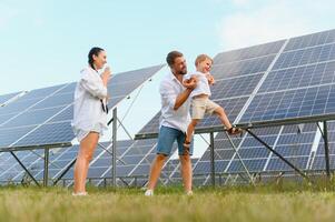 joven familia con un pequeño niño en su brazos en un antecedentes de solar paneles un hombre y un mujer Mira a cada otro con amor. solar energía concepto. foto