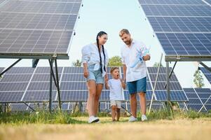 un amplio Disparo de un contento familia en pie juntos y sonriente a cámara con un grande solar panel en antecedentes foto