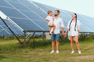 joven familia con un pequeño niño en su brazos en un antecedentes de solar paneles un hombre y un mujer Mira a cada otro con amor. solar energía concepto. foto