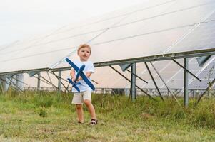 Little happy boy playing with toy airplane near solar panels. photo