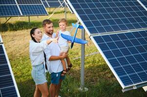 joven familia de Tres es agachado cerca fotovoltaica solar panel, pequeño chico y padres. moderno familia concepto. el concepto de verde energía foto