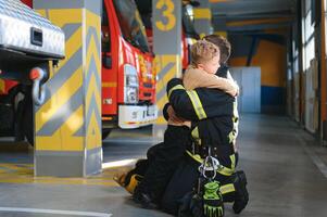 A firefighter take a little child boy to save him. Fire engine car on background photo