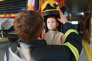 A fireman shows his work to his young son. A boy in a firefighter's helmet photo